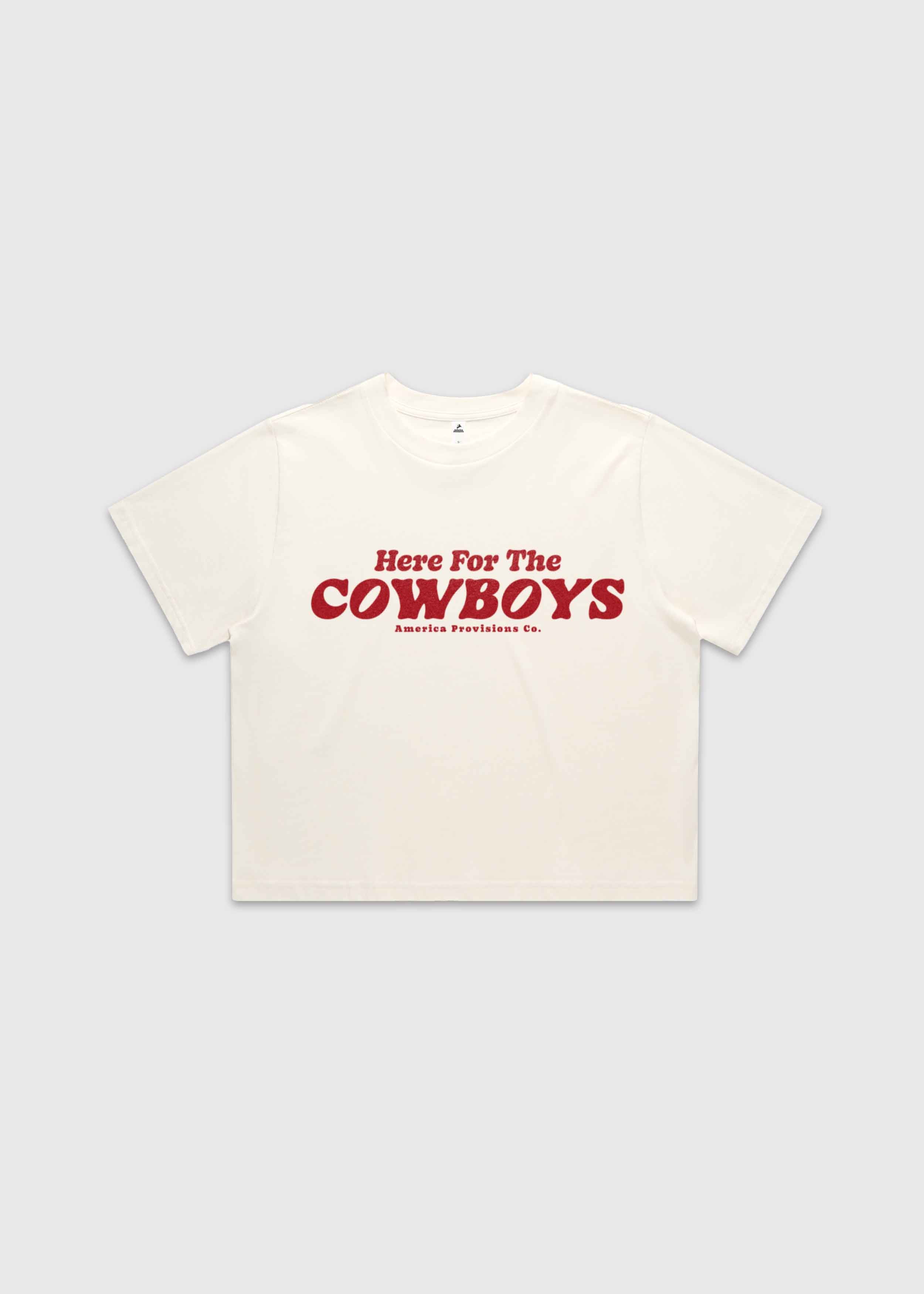 Ecru cropped t-shirt with bold red “Here For The Cowboys” Western graphic, structured boxy fit, heavy cotton fabric, America Provisions apparel product photo on a neutral background.
