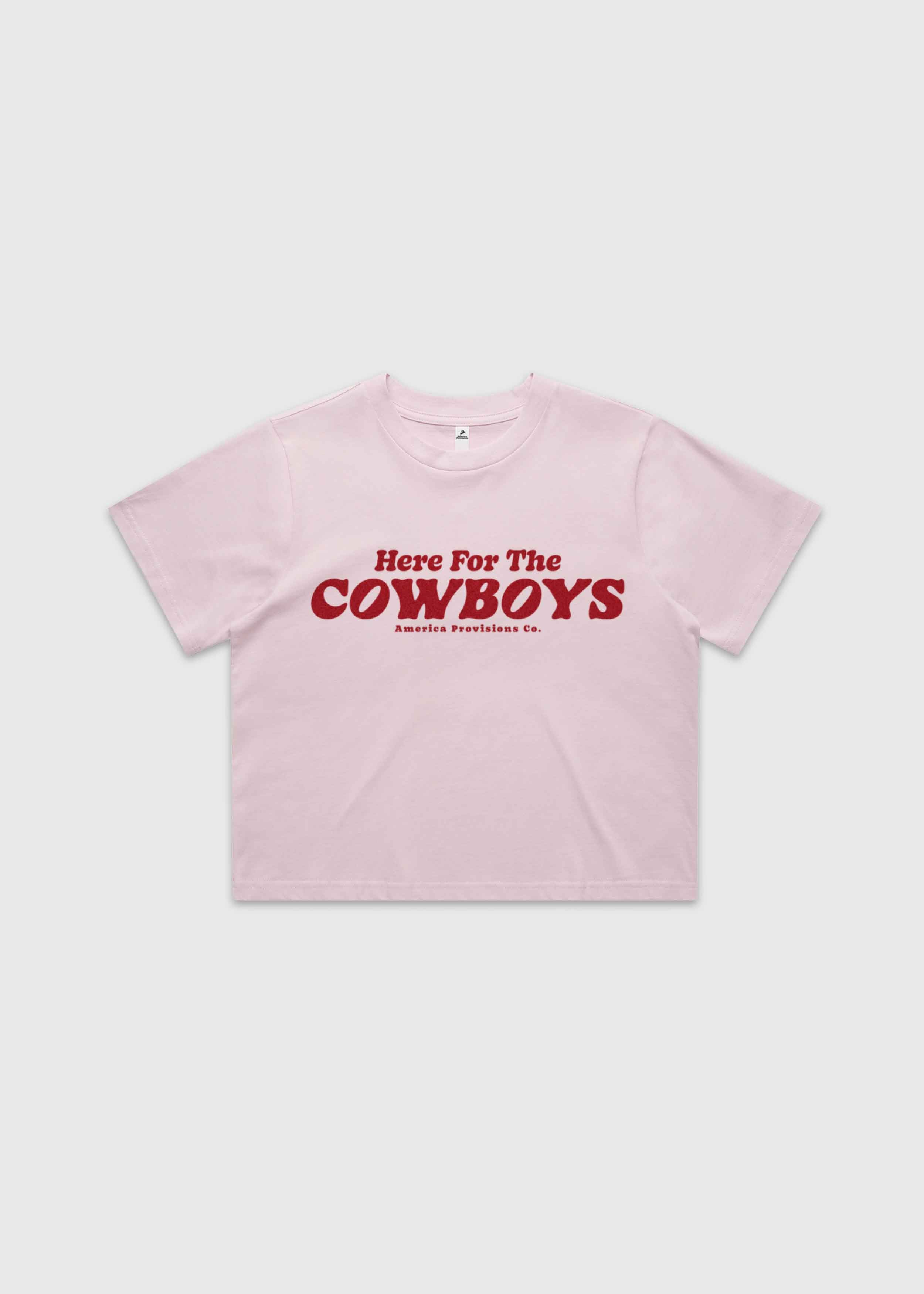 Pink cropped t-shirt with bold red “Here For The Cowboys” Western graphic, structured boxy fit, heavy cotton fabric, America Provisions apparel product photo on a neutral background.