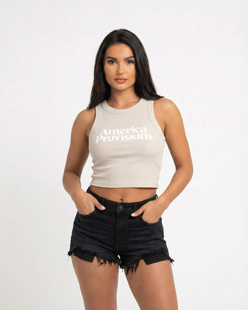 Ecru crop top with America Provisions logo on. Blonde model is wearing the crop top and denim shorts