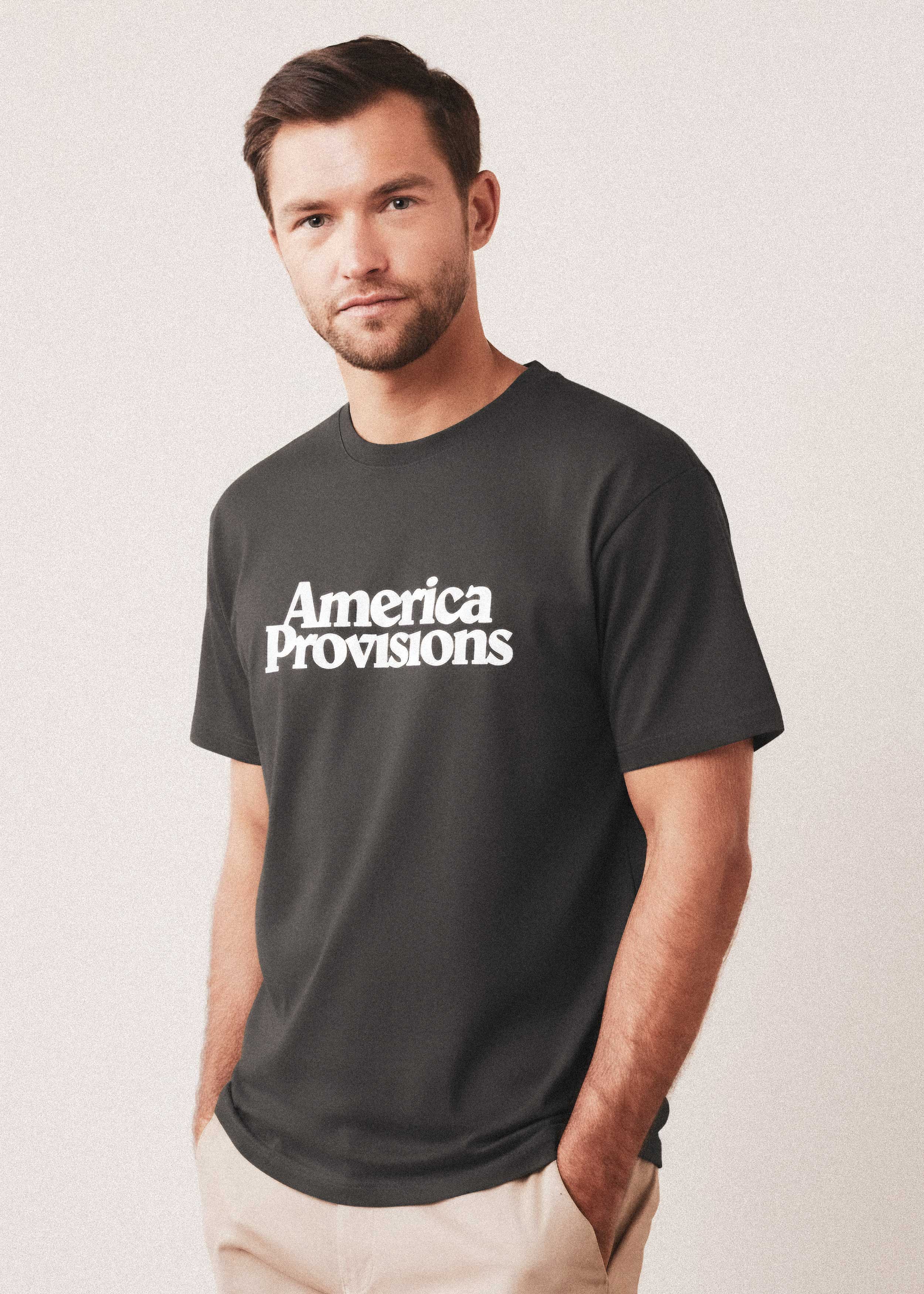 Man wearing a coal colored t-shirt with 'America Provisions' text on a light background