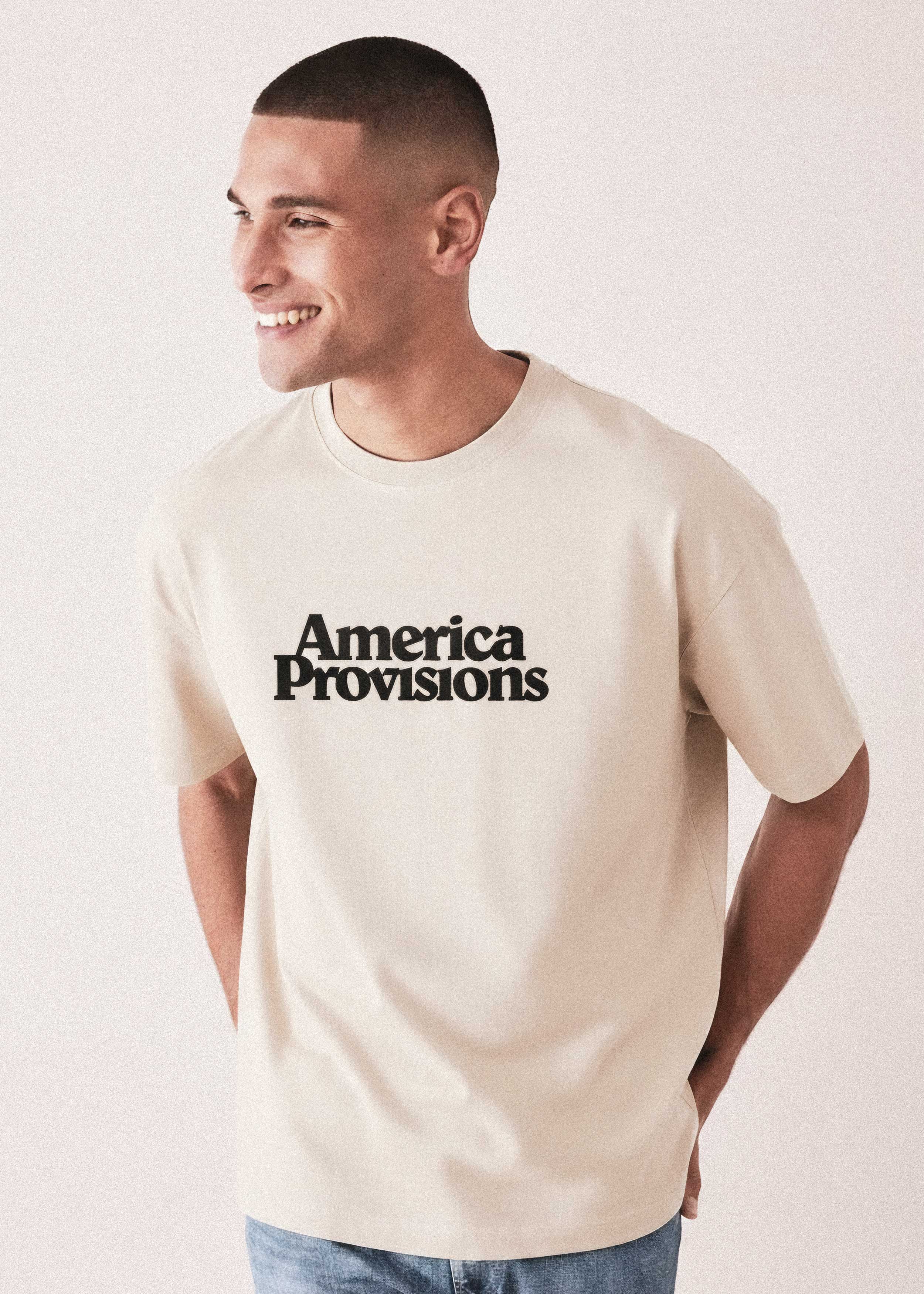 Man wearing a beige t-shirt with 'America Provisions' text on a light background