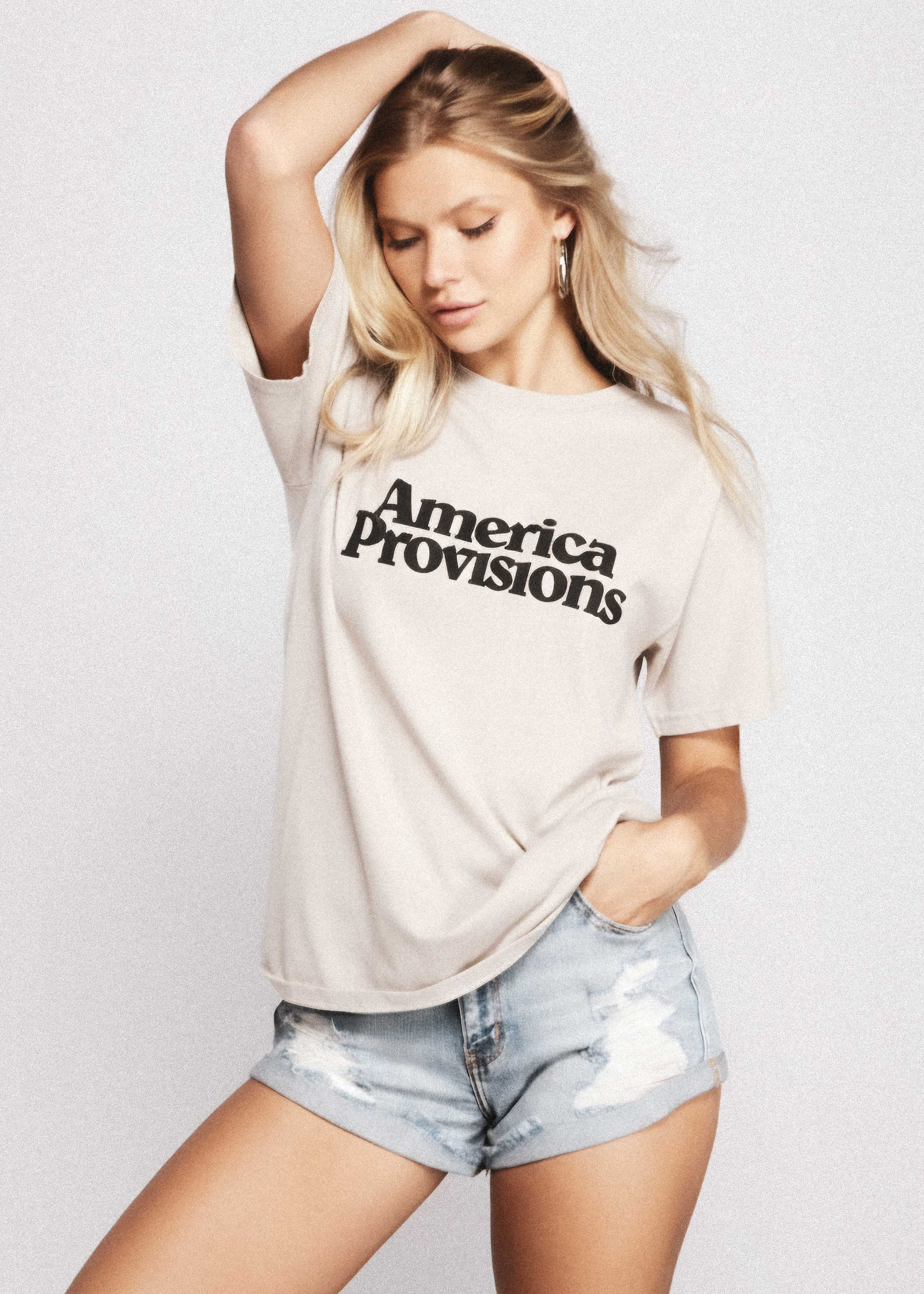 Woman wearing a 'America Provisions' t-shirt and denim shorts on a plain background