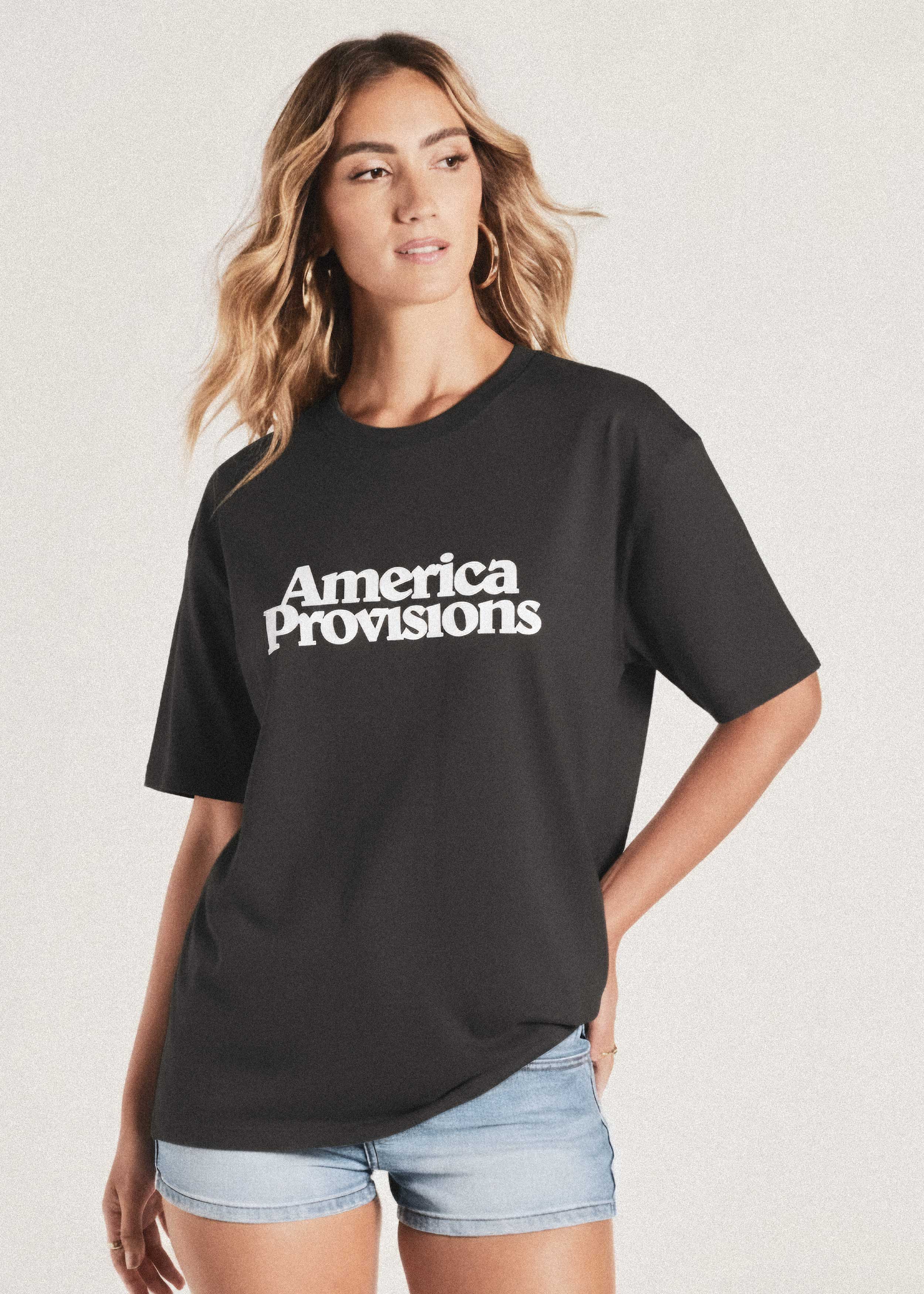 Woman wearing a coal colored t-shirt with 'America Provisions' text on a plain background
